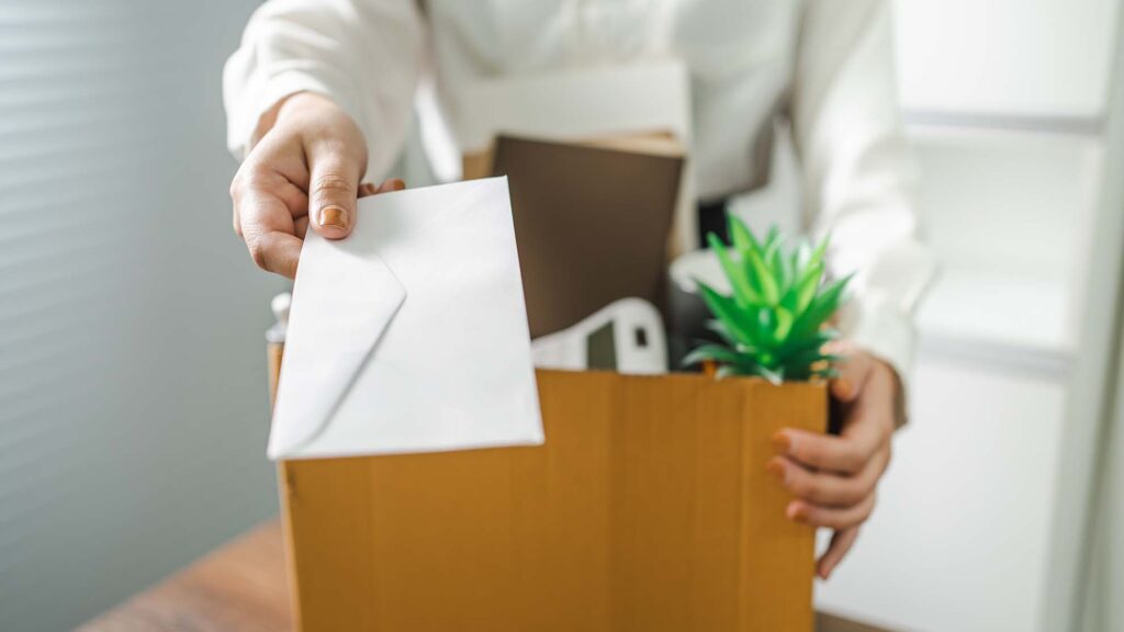 Woman Handing in Resignation Letter with Box of Personal Items from Desk